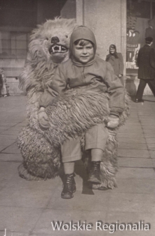 Dziecko z mężczyzną w kostiumie białego niedźwiedzia na tle Powszechnego Domu Towarowego Wola